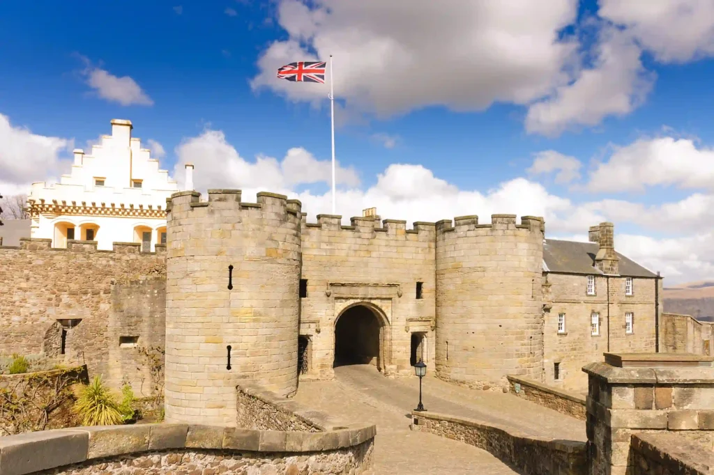 Historic stone castle entrance with British flag, under a blue sky with clouds. Ideal for exploring heritage sites.