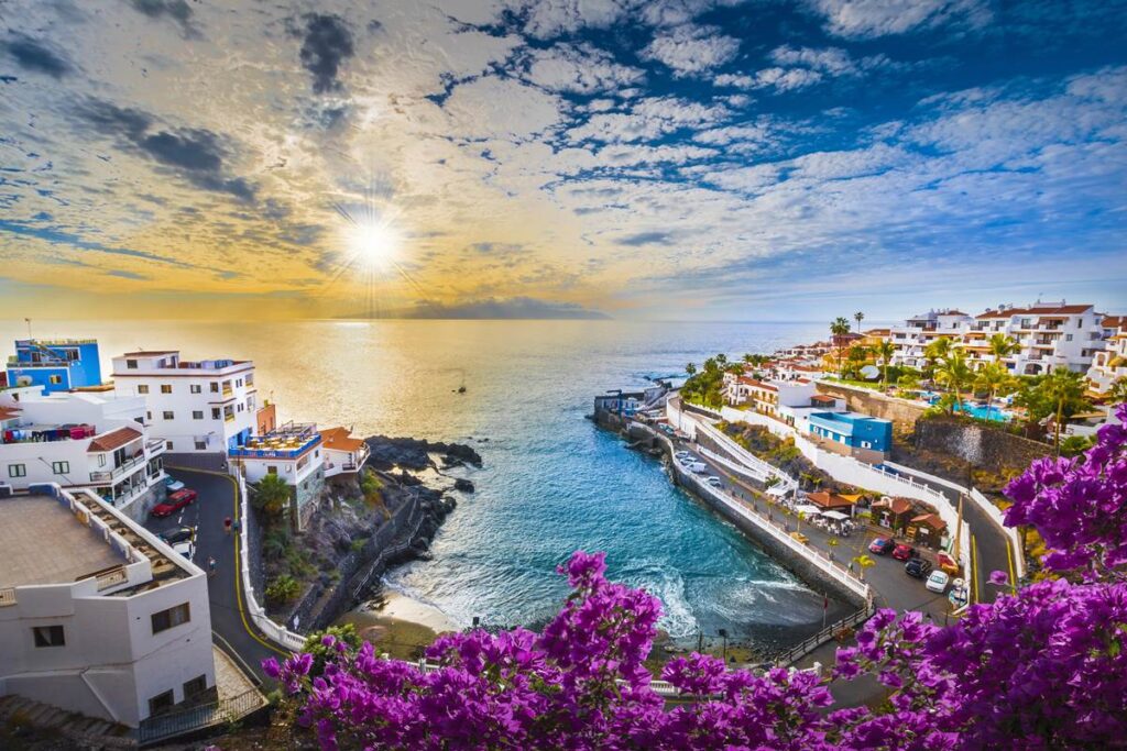 Colorful coastal town at sunset with ocean view, vibrant flowers, and charming white buildings.