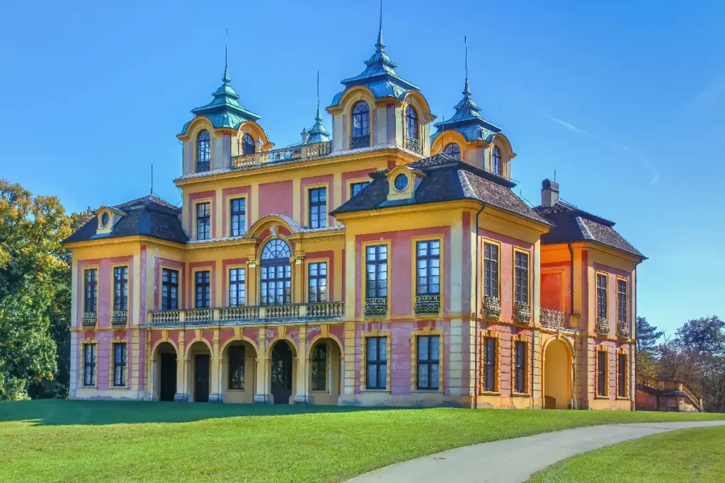 Baroque-style mansion with colorful exterior and ornate architecture, surrounded by lush greenery under a clear blue sky.