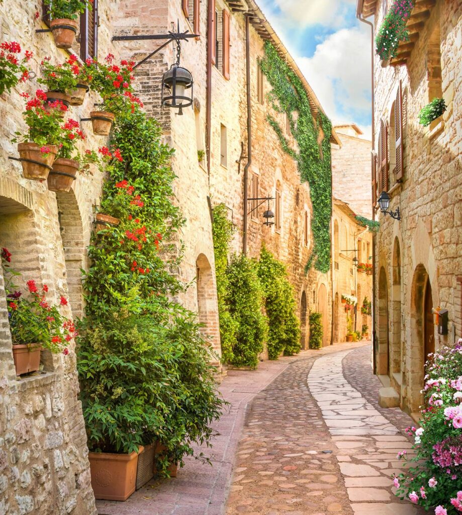 Charming narrow cobblestone street in quaint Italian village with flower-covered stone buildings and lanterns.