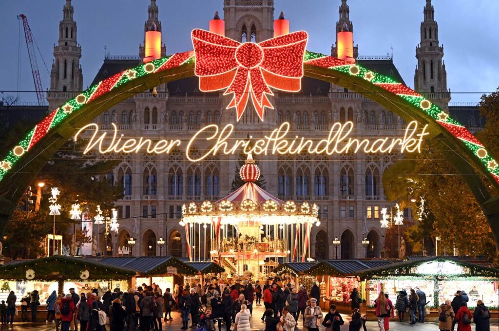 Festive Wiener Christkindlmarkt with carousel, lights, and people in front of illuminated city hall in Vienna.